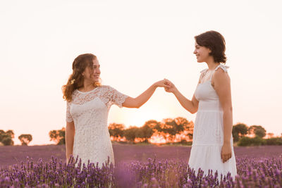 Smiling lesbian couple holding hands standing on flower field