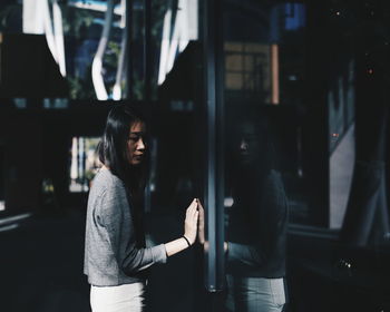 Woman standing by glass window in city