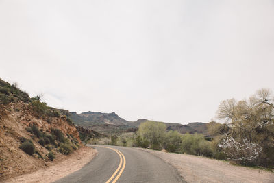 Empty road by mountains against clear sky