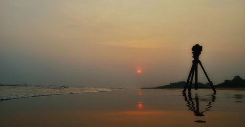 Reflection of silhouette photographing on sea against sky during sunset