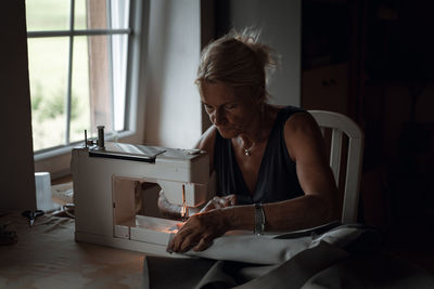 Side view of woman using sewing machine at home