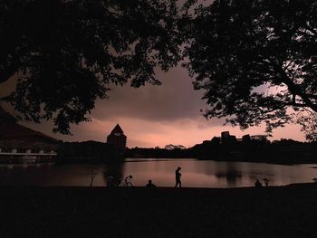 Silhouette people by lake against sky during sunset