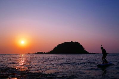 Silhouette person on paddleboard in sea against sky during sunset