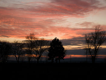 Silhouette trees on field against romantic sky at sunset