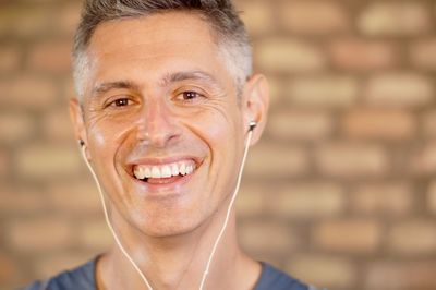 Portrait of smiling mature man wearing headphones against wall