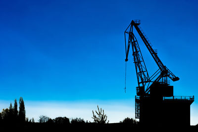 Low angle view of crane at construction site against blue sky