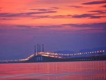 Illuminated bridge over river against sky at sunset