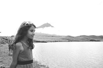 Side view of girl looking away while standing at lakeshore against clear sky