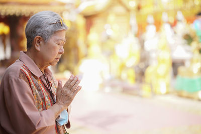 Old asian elder senior woman traveler tourist praying at buddhist temple.