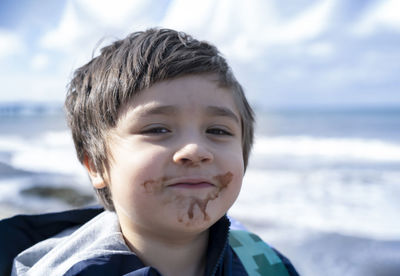 Close-up portrait of boy with messy mouth against sea