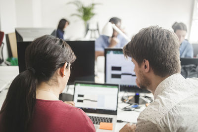 Male and female colleagues discussing over laptop on desk in creative office