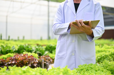 Midsection of doctor standing in greenhouse