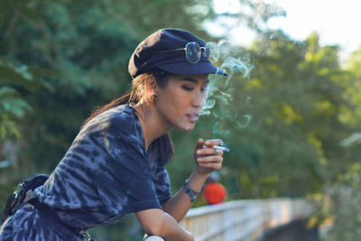 Young woman smoking cigarette against trees