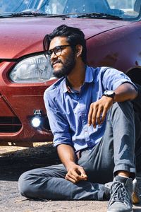 Full length of man sitting by car on road