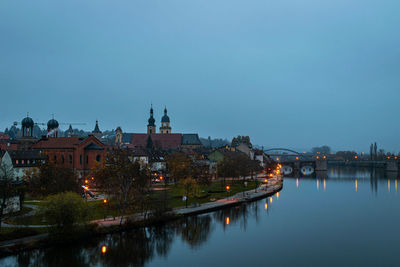 River by illuminated buildings against clear sky at dusk