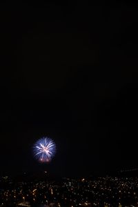 Firework display in city against clear sky at night