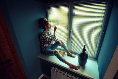 Woman sitting on window sill at home