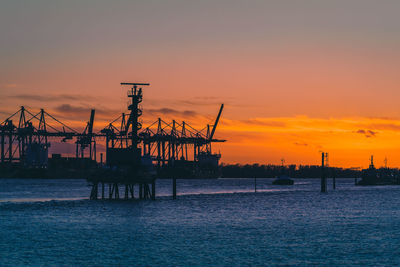 Silhouette cranes at commercial dock against sky during sunset