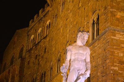 Low angle view of statue against building in city at night