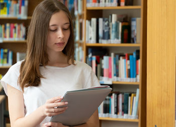 Teenage girl holding file while standing in library