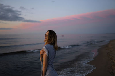 Woman looking away while standing at beach during sunset