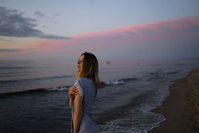 Rear view of woman standing at beach during sunset