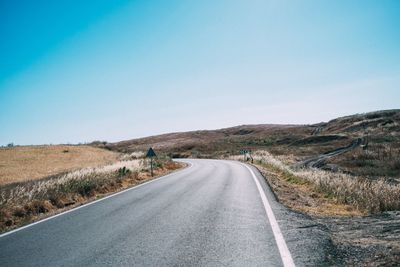 Empty road leading towards mountains against blue sky