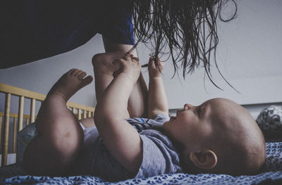 Cropped image of woman playing with baby boy lying on bed