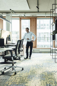 Male entrepreneur with hand on hip leaning on chair in office