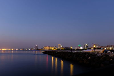 Illuminated city at waterfront during sunset