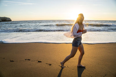 Teenage girl running on beach at sunset