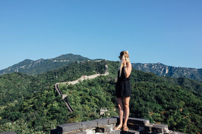 Rear view of young woman standing on mountain against clear sky