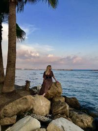 Woman sitting on rock at sea against sky