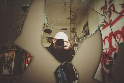 Reflection of man on broken mirror while photographing using camera
