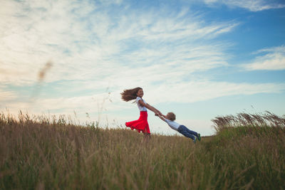 Girl carrying brother on field against sky