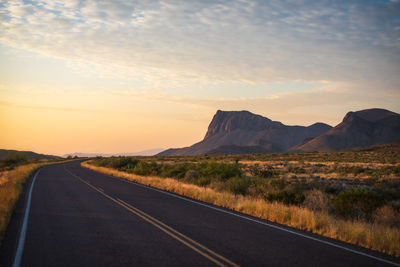 Road leading towards mountains against sky during sunset