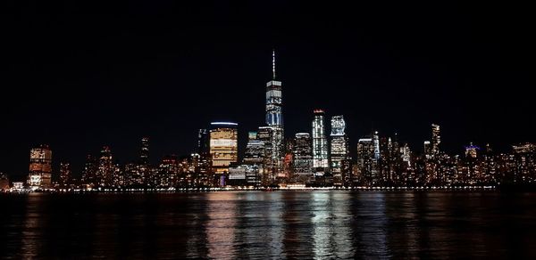 Illuminated buildings by river against sky at night