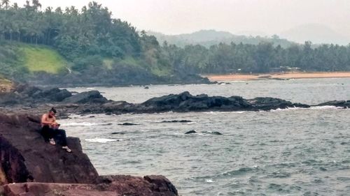 Man on rock by sea against sky