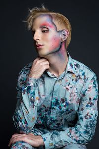 Young man with make-up in floral clothing against black background