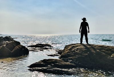 Man standing on rock at beach against sky