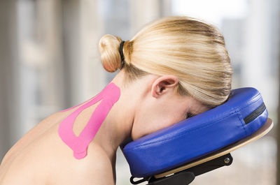 Side view of mature woman with pink kinesio tape sitting on neck massage chair