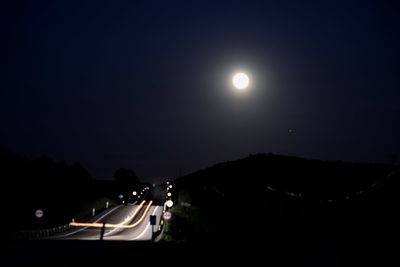 Cars on illuminated road against clear sky at night