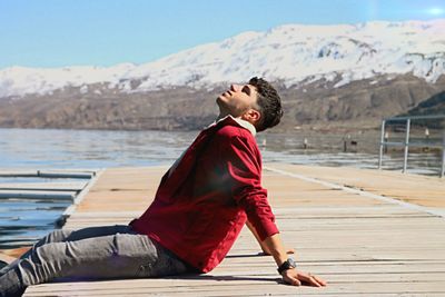 Side view of young man sitting on pier against mountain