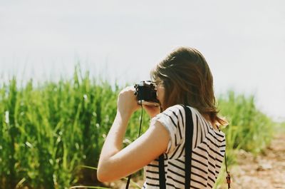 Side view of young woman photographing field against sky