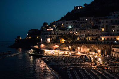 Illuminated buildings by sea against sky at night