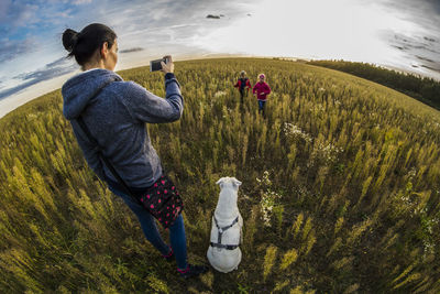 Fish-eye lens view of mother photographing children running on field