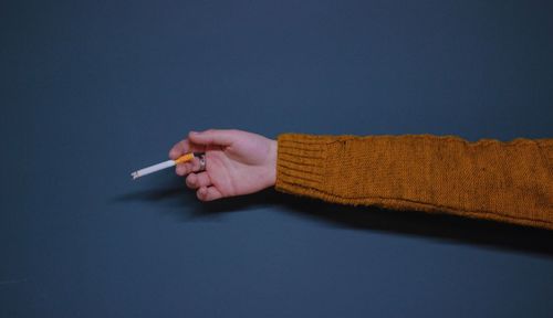 Close-up of hand holding cigarette over gray background