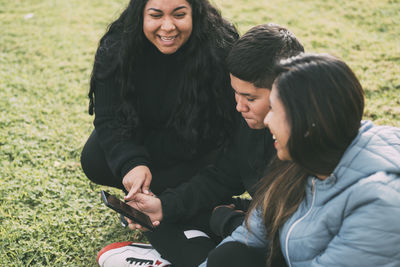 Group of latinos laughing sitting on the ground in a park with a smartphone