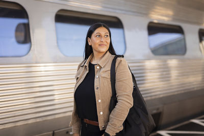 Smiling mid adult woman standing at train station looking away