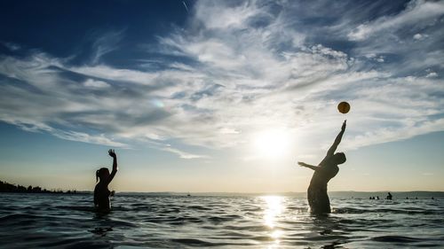 Friends playing with beach ball in sea during sunny day